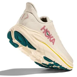 A HOKA running shoe featuring off-white uppers, pink branding, yellow accents, and a thick sole with teal tread for enhanced support and traction.
